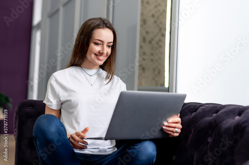 Young beautiful woman using a laptop computer at home. Black sofa. Smiling young woman with laptop. © Vadim