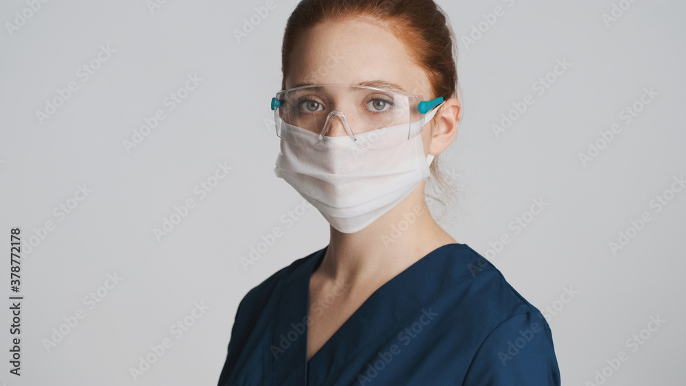 Young professional doctor in protective eyeglasses and medical mask intently looking in camera isolated. Safety first concept Young professional doctor in protective eyeglasses and medical mask intently looking in camera isolated. Safety first concept