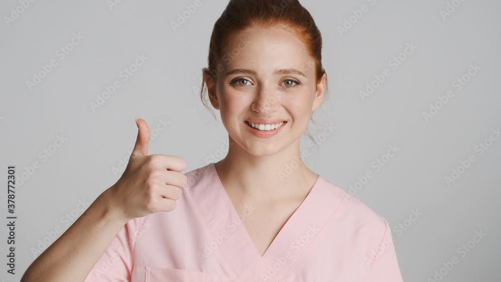 Young beautifu nurse in uniform happily showing thumb up on camera over white background. Like it expression Young beautifu nurse in uniform happily showing thumb up on camera over white background. Like it expression