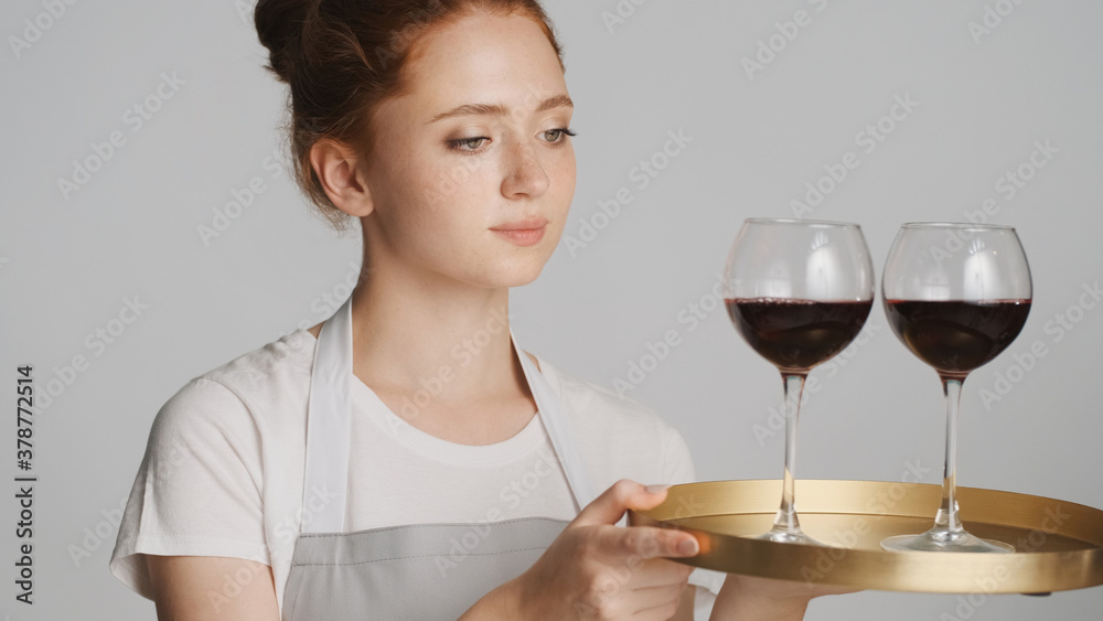 Young waitress in apron intently holding tray with wine over white background Young waitress in apron intently holding tray with wine over white background