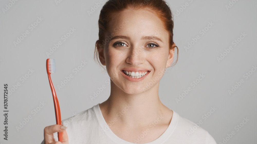 Beautiful redhead girl happily posing with toothbrush and smiling on camera over white background Beautiful redhead girl happily posing with toothbrush and smiling on camera over white background