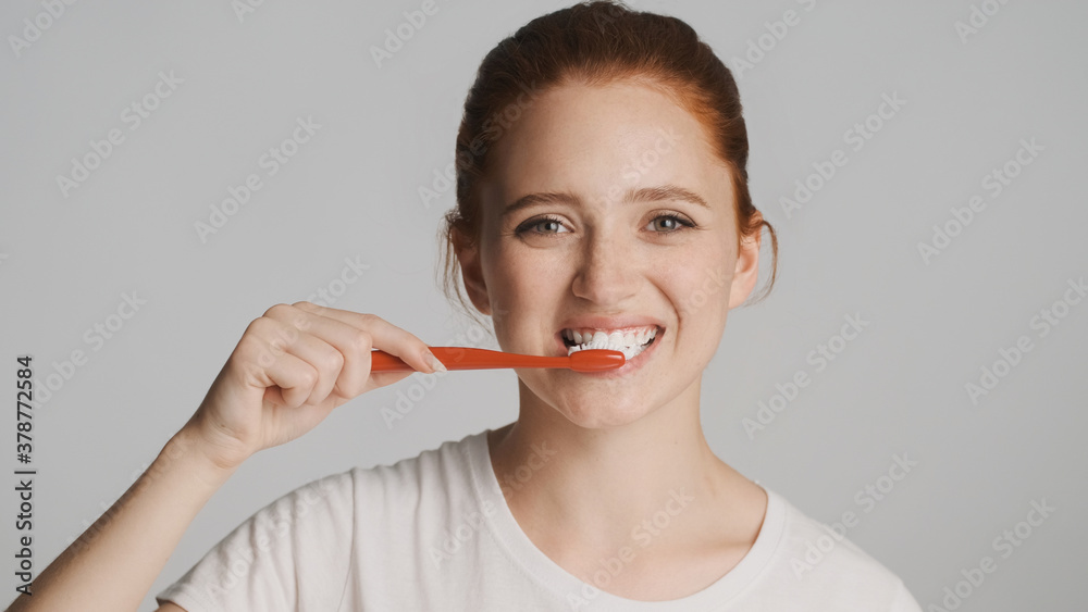 Portrait of beautiful girl intently looking in camera brushing teeth over white background Portrait of beautiful girl intently looking in camera brushing teeth over white background