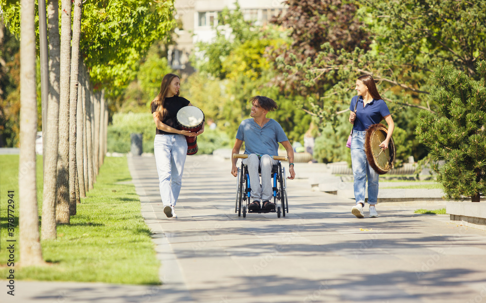 Summer. Happy caucasian handicapped man on a wheelchair spending time with friends playing live instrumental music outdoors. Concept of social life, friendship, possibilities, inclusion, diversity.