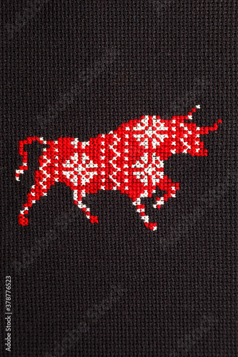 Bull with a Christmas ornament embroidered with red threads on a black background. Symbol of 2021.