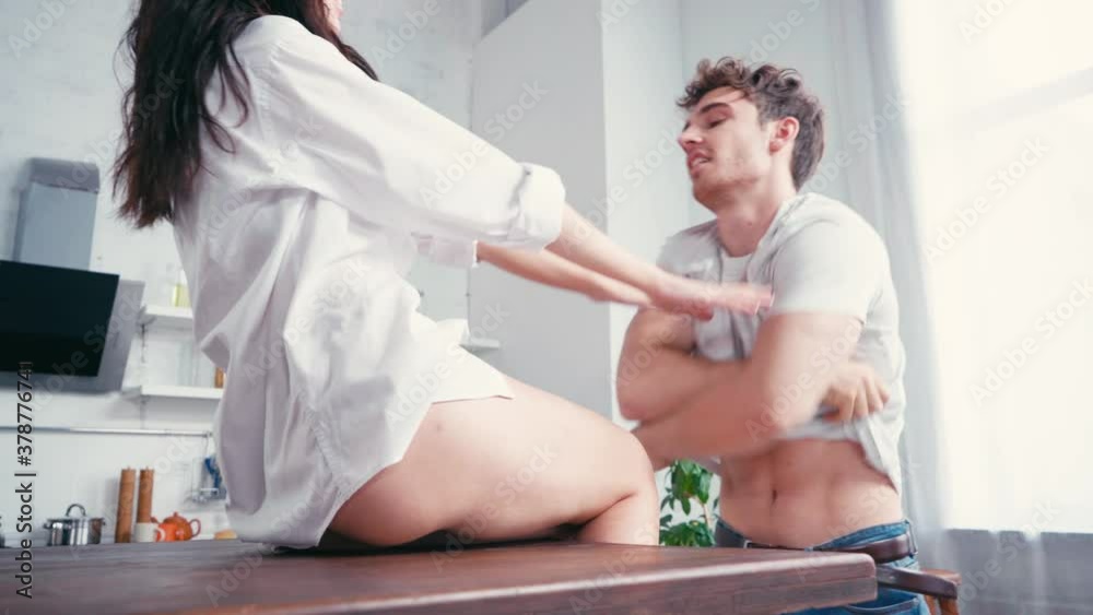 Man taking off t-shirt near sexy girlfriend on table in kitchen 