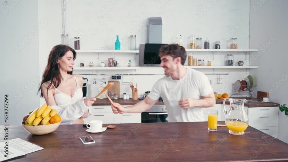 Young couple having fun with spatulas near coffee and orange juice in kitchen Young couple having fun with spatulas near coffee and orange juice in kitchen
