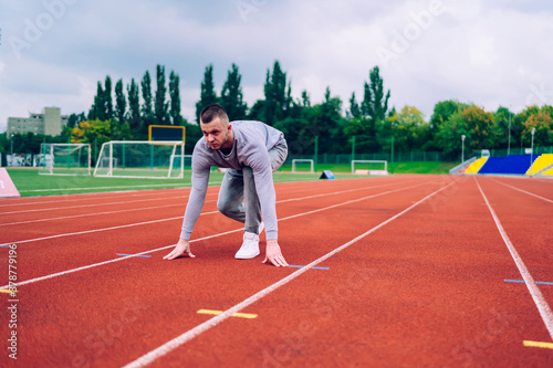 Handsome determined male runner standing on start point on stadium prepare for running distance, serious caucasian man athlete looking straight for begin fast cardio workout for reaching goals