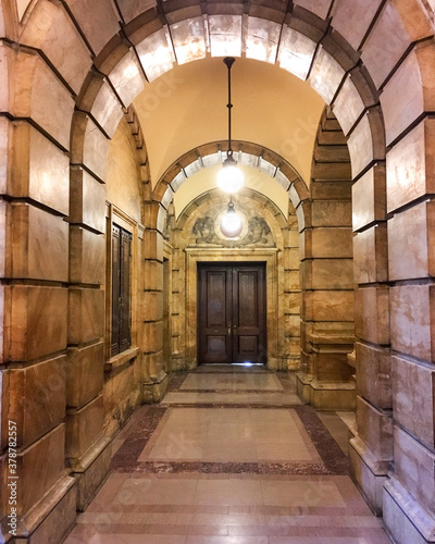 Hallway or corridor in historic public building with long aisles, archs and archways, wooden doors and ceiling lights photo