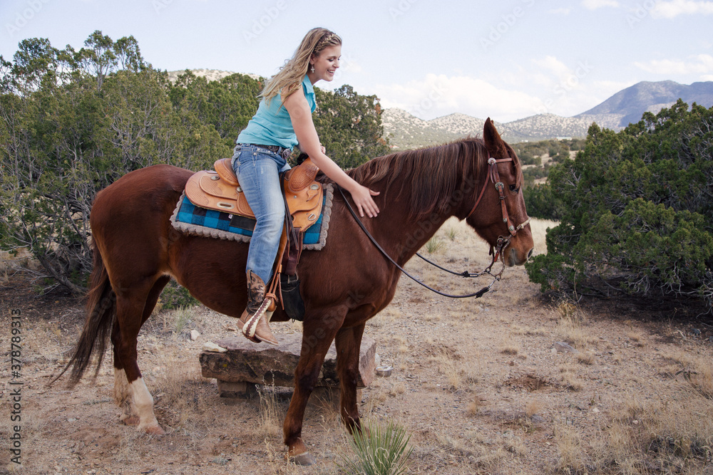 Southwestern theme with a Cowgirl with cowboy hat and chaps Riding brown Horse in the hills and ranch Outdoors in New Mexico Southwestern theme with a Cowgirl with cowboy hat and chaps Riding brown Horse in the hills and ranch Outdoors in New Mexico