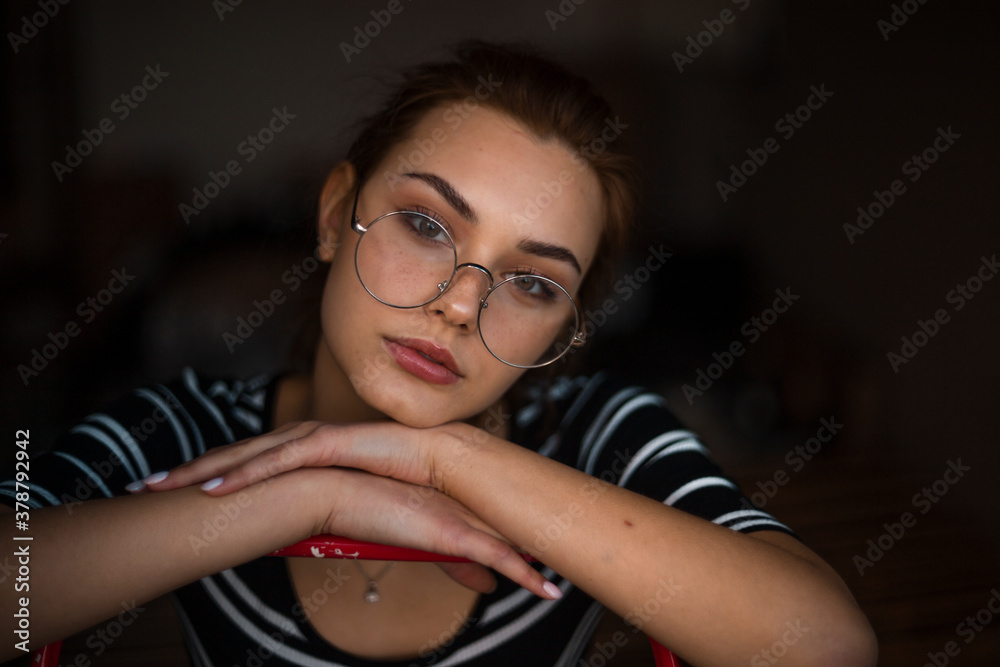 A nice girl is spectacled in a dark apartment. Laid a head on hands, sad