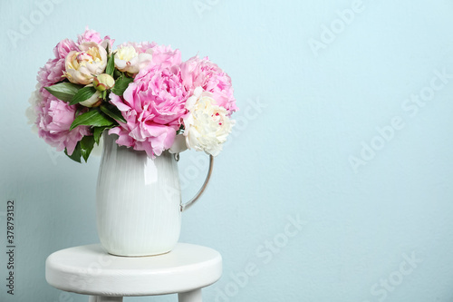 Beautiful peonies in jug on white stool against light blue background. Space for text