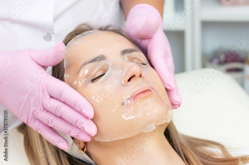cosmetologist applies a hydrogel mask to a young woman on her face. The procedure by a beautician. Relax