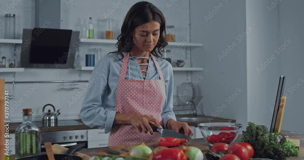 Woman in apron cutting salad near ripe vegetables on table Woman in apron cutting salad near ripe vegetables on table