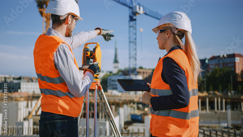 Construction Worker Using Theodolite Surveying Optical Instrument for Measuring Angles in Horizontal and Vertical Planes on Construction Site. Engineer and Architect Using Tablet Next to Surveyor. photo