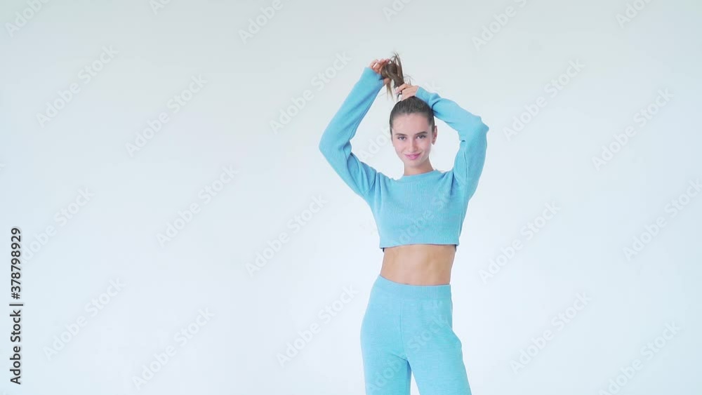 Portrait of a young attractive fashion model woman with natural long hair in blue clothes on a white background. posing and looking at the camera. shakes hands holding hair up. Makeup natural beauty Portrait of a young attractive fashion model woman with natural long hair in blue clothes on a white background. posing and looking at the camera. shakes hands holding hair up. Makeup natural beauty
