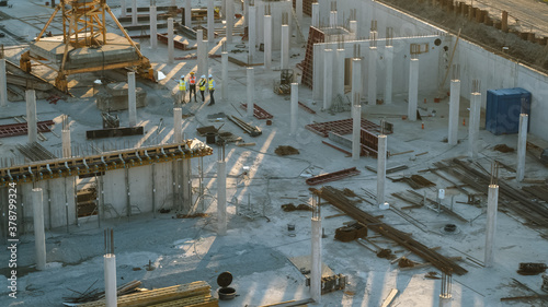 Aerial Shot of a New Constructions Development Site with Diverse team of Engineers and Architects Discussing Real Estate Projects. Heavy Machinery and Construction Workers are Working in the Area.