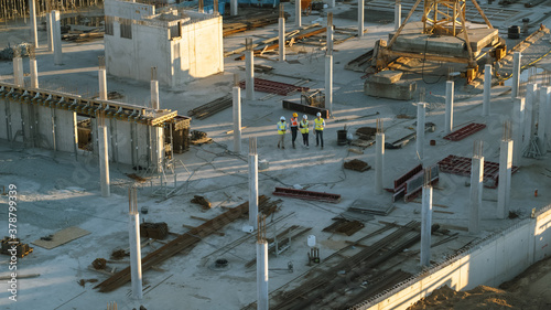 Aerial Shot of a New Constructions Development Site with Diverse team of Engineers and Architects Discussing Real Estate Projects. Heavy Machinery and Construction Workers are Working in the Area.