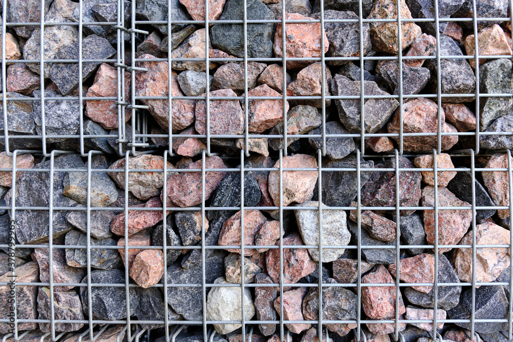 The wall of large granite stones in the grid. The texture of the stone wall is covered with a metal mesh.