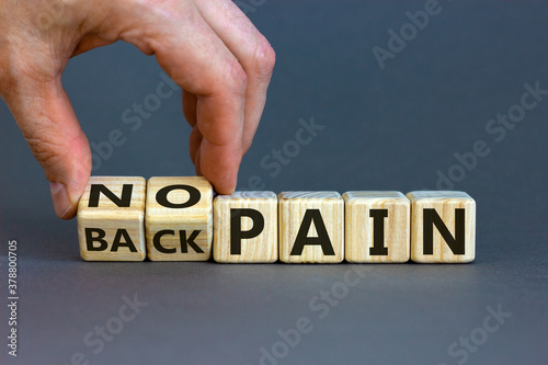 Male hand turns a cube and changes the expression 'back pain' to 'no pain'. Beautiful grey background, copy space. Medical concept.