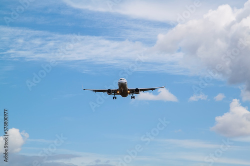 white passenger plane comes in to land with natural background of white clouds and blue sky