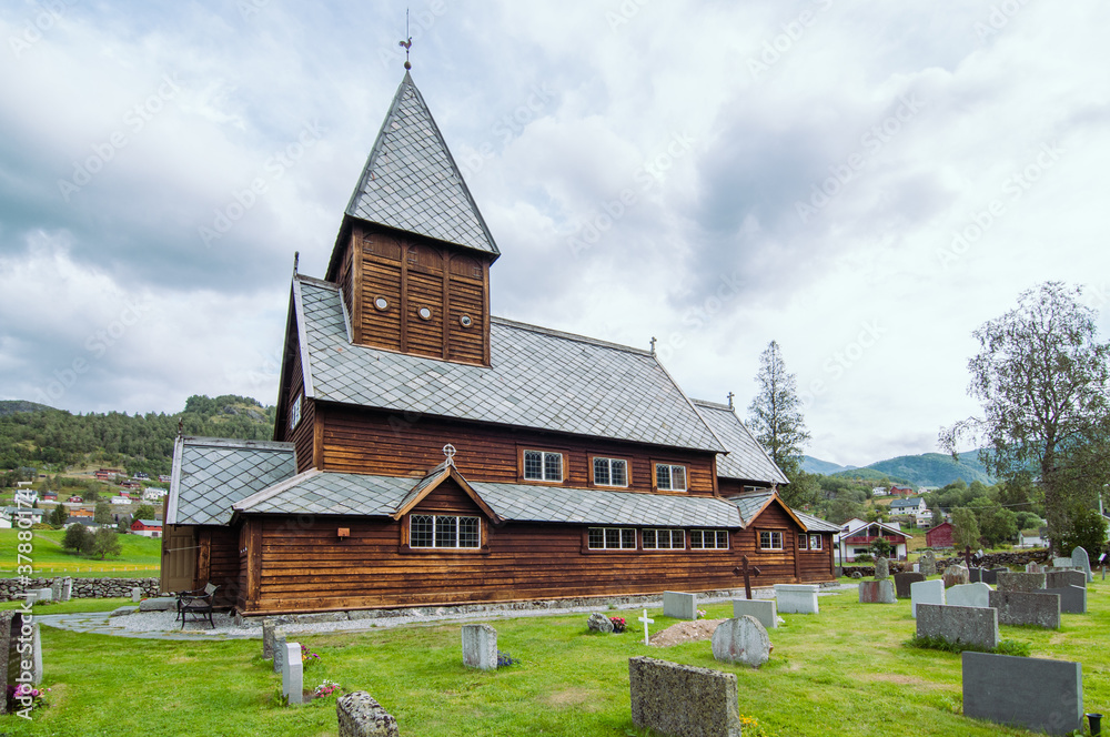 Horizontal photo of a Norwegian wooden stave church with its graveyard in a cloudy day. Røldal, Norway.