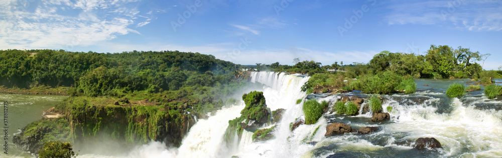 Large nature panorama of Iguacu (Iguazu) waterfall cascade on border of Brazil and Argentina. Amazing view of falls Cataratas in bright Sunny weather. Concept of travel. Copyright space for site