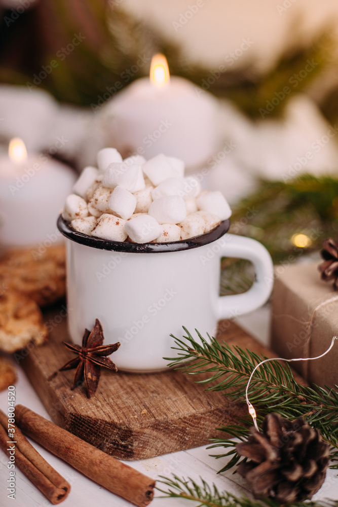 Enamelled cup of hot cocoa or coffee with marshmallows and cookies. Around the tree branches, gifts and burning candles. Christmas mood. Postcard or winter background. Enamelled cup of hot cocoa or coffee with marshmallows and cookies. Around the tree branches, gifts and burning candles. Christmas mood. Postcard or winter background.