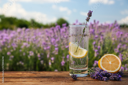Lemonade with lemon slice and lavender flowers on wooden table outdoors, closeup. Space for text