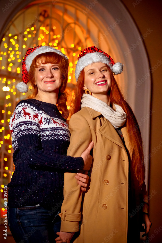 mother and daughter in winter clothes on the background of a shop window with Christmas lights