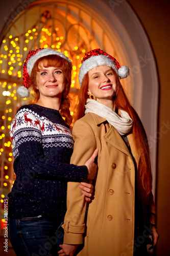 mother and daughter in winter clothes on the background of a shop window with Christmas lights