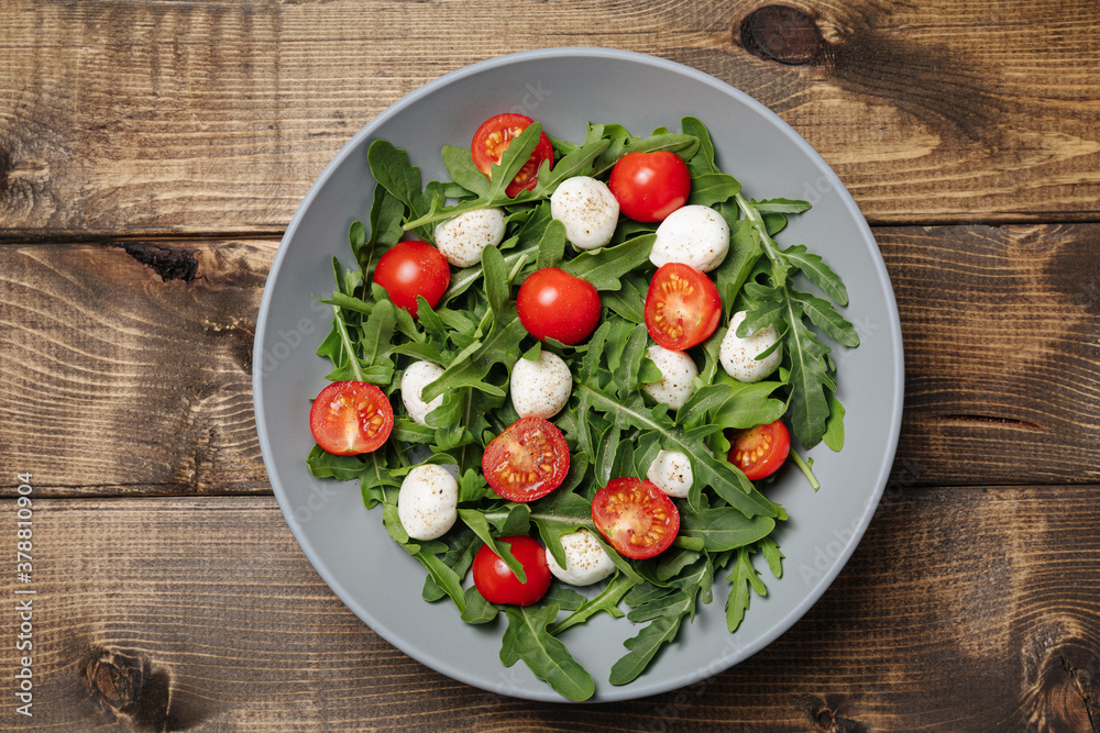 Diet and healthy salad with arugula, cherry tomatoes, mozzarella cheese on wooden background