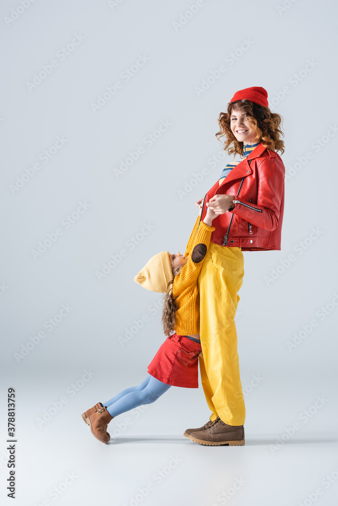 side view of mother and daughter in colorful red and yellow outfits playing on grey background side view of mother and daughter in colorful red and yellow outfits playing on grey background