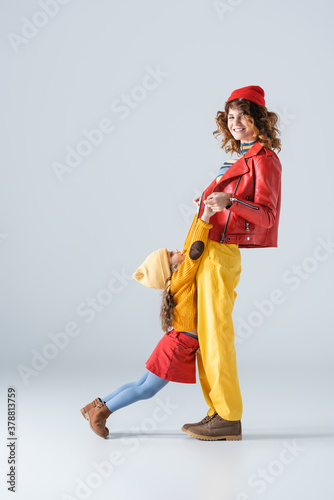 side view of mother and daughter in colorful red and yellow outfits playing on grey background