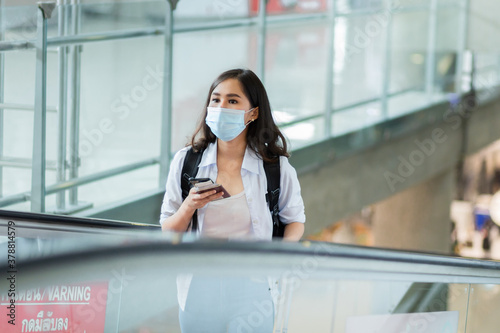 Asian traveler women using smartphone while standing on the sliding walkway in airport.