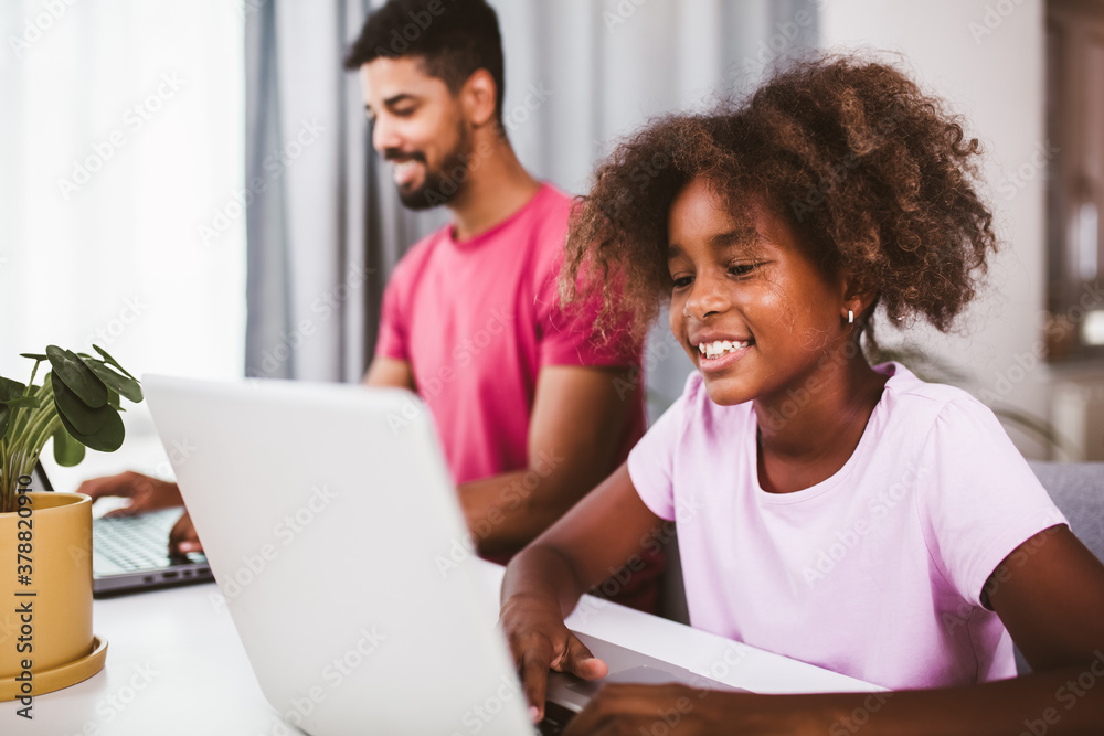 Father using laptop while his daughter is doing homework in the living room. Father using laptop while his daughter is doing homework in the living room.