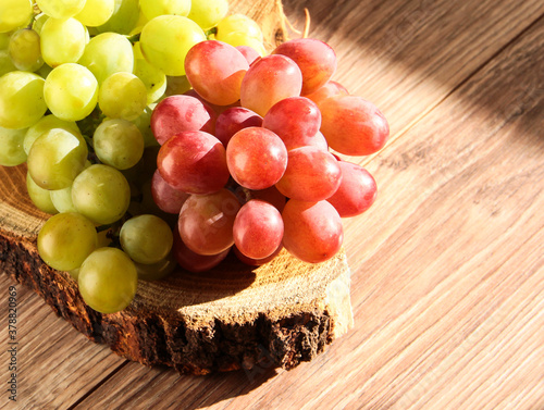 Clusters of white and pink grapes on a wooden background. On the bark are bunches of grapes. photo