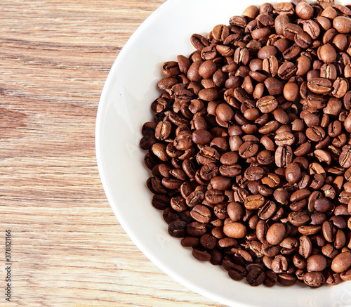 Coffee beans in a white bowl on a wooden background.