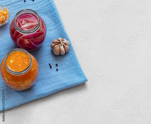 Two jars with fermented vegetables: cabbage, carrots and onions, spices on a blue napkin. Gray background. View from above. photo