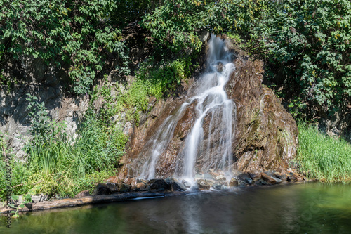An artificial waterfall flowing down a rock into a reservoir. There are green trees around.