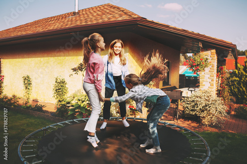 Happy three children are jumping on a trampoline in the garden near their house.