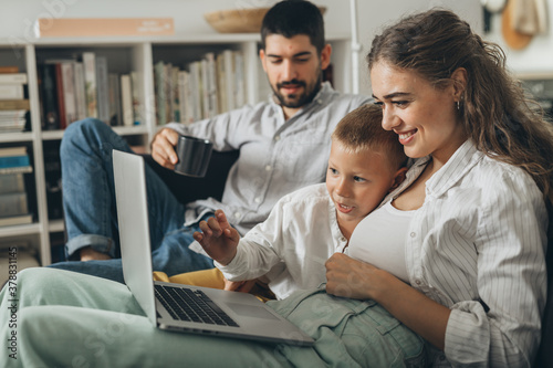happy young family using laptop computer sitting on the sofa at home