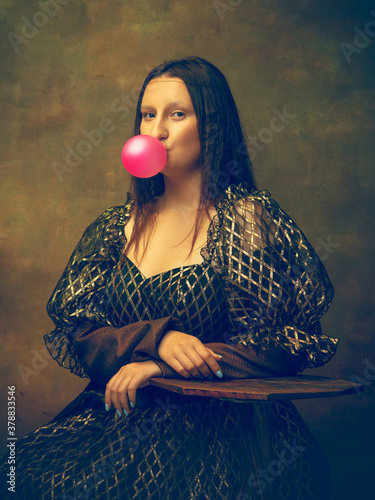 Bubble gum. Young woman as Mona Lisa, La Gioconda isolated on dark green background. Retro style, comparison of eras concept. Beautiful female model like classic historical character, old-fashioned. photo