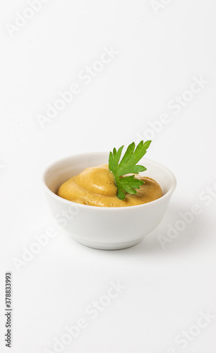 Mustard sauce decorated with parsley in a small white bowl on a white background