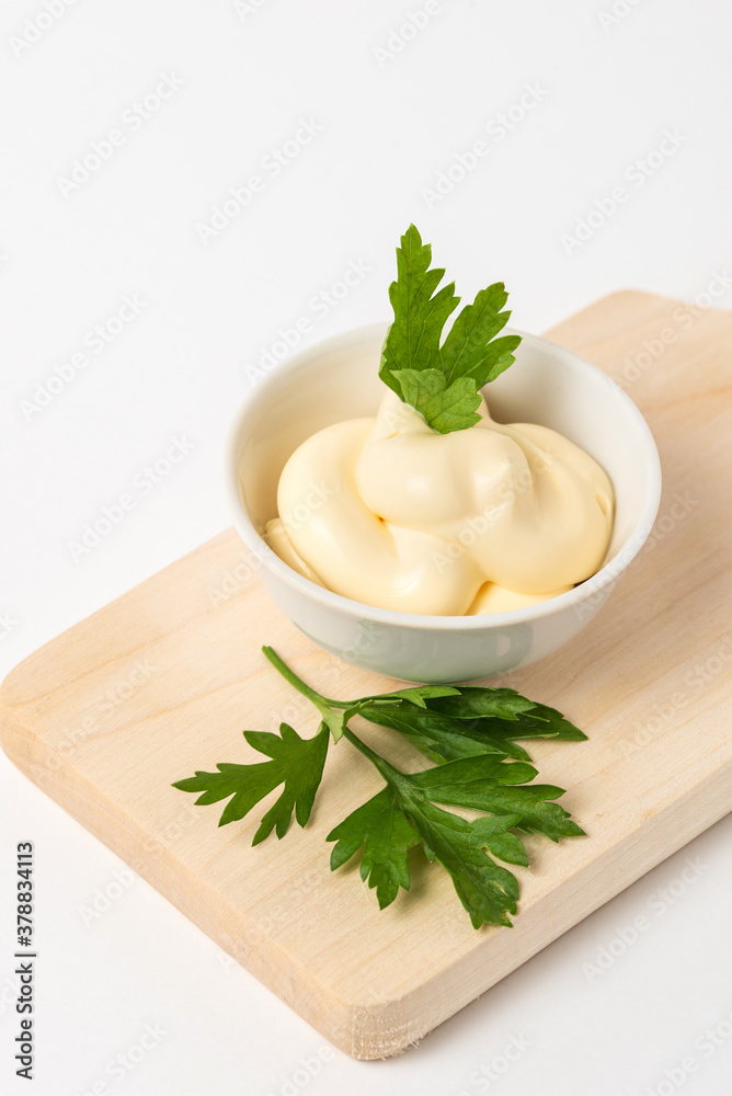 Mayonnaise sauce garnished with parsley in a small white bowl on a wooden cutting Board on a white background Mayonnaise sauce garnished with parsley in a small white bowl on a wooden cutting Board on a white background