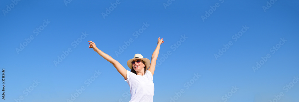 Young girl with raised hands in a hat against a blue sky background