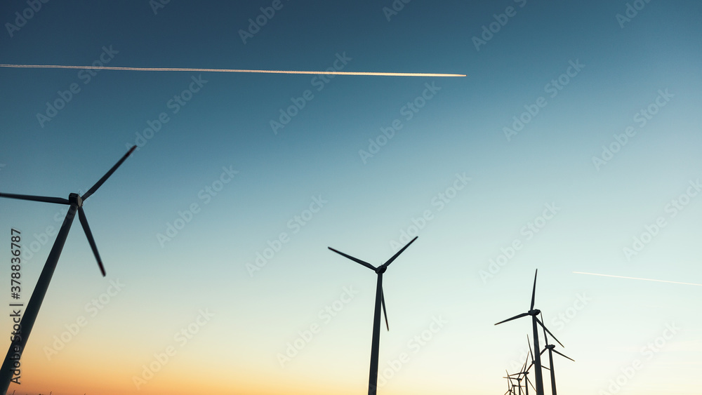 Fototapeta premium Wind Turbines at Dusk. Landscape sunset with windmills. Renewal source of electricity. Wind turbines field new technology for clean energy on mountain, sunset view with colorful twilight on sky.