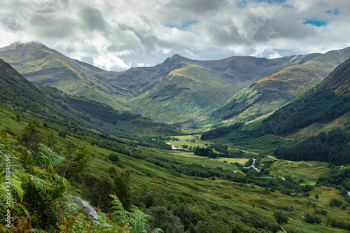 Dramatic Glen Nevis view with mountains in distance and lush valley, cloudy with patches of blue sky