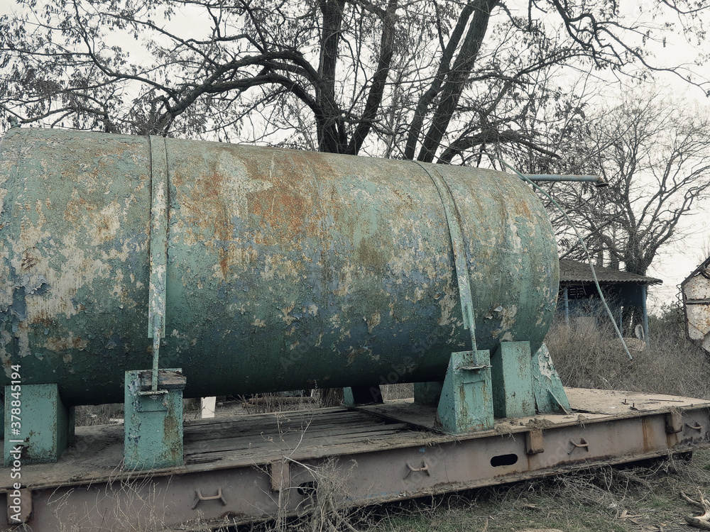 Large rusty metal water tank with remains of blue and green paint. Old big rusty automobile water tank with traces of rust. Abandoned waste rusty painted metal car tank, water barrel. Large rusty metal water tank with remains of blue and green paint. Old big rusty automobile water tank with traces of rust. Abandoned waste rusty painted metal car tank, water barrel.