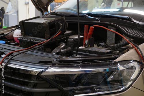 A modern car in a car service at a diagnostic post. The hood is open on the vehicle and diagnostic equipment is connected.