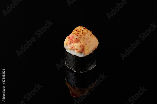 Maki - smoked eel, cream cheese, avocado, masago, sesame seeds, tempura, Spicy sauce on a black background